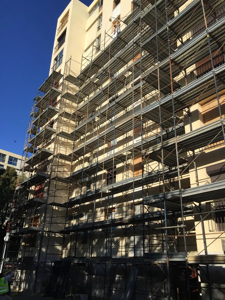 Façade d’immeuble de grande hauteur sous échafaudage, enduit jaune clair, ciel bleu