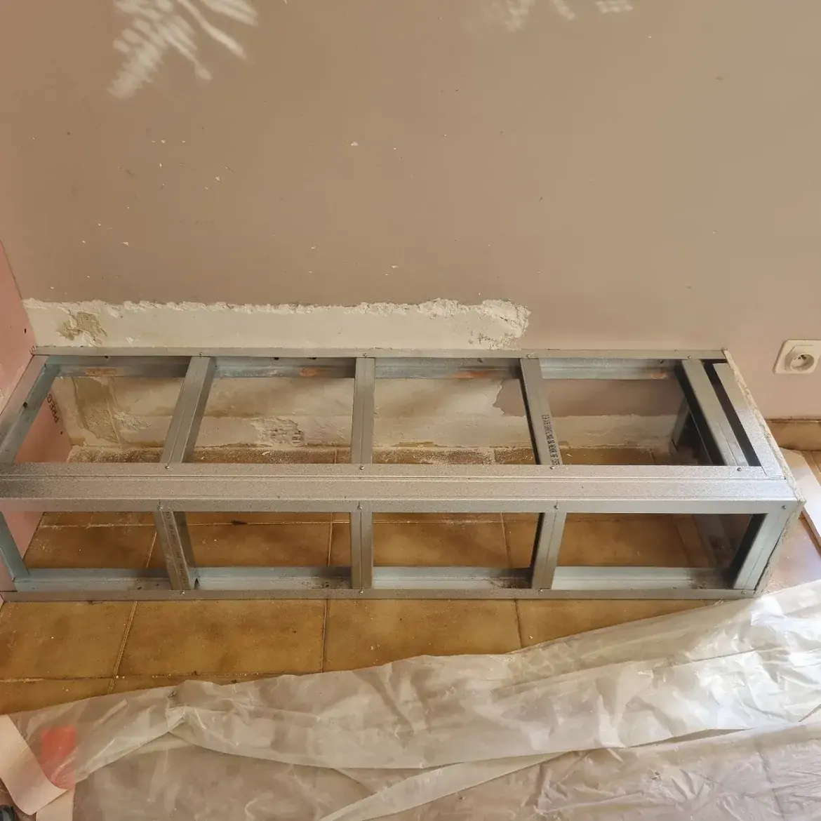 Ossature métallique d’un banc en plaques de plâtre, posée au pied d’un mur