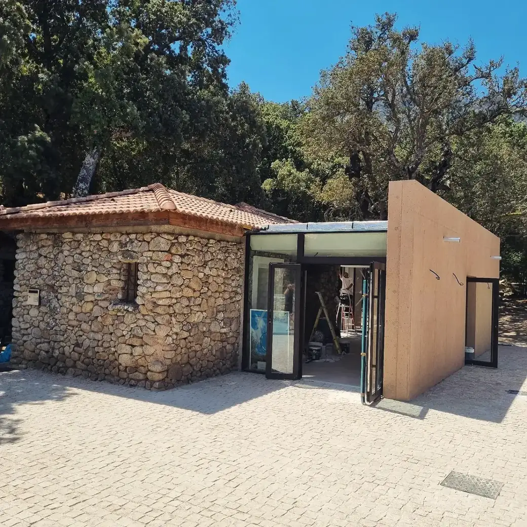 Entrée vitrée d’un pavillon à côté d’un mur de pierre, un peintre au travail à l’intérieur