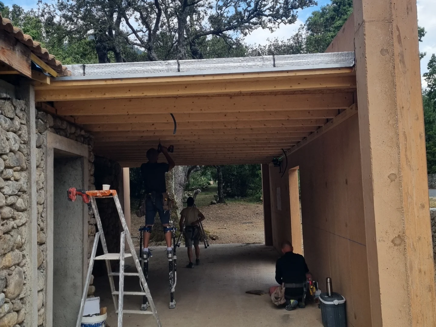 Équipe au travail sous le plafond bois d’un auvent, entre un mur de pierre et un mur en panneaux bois