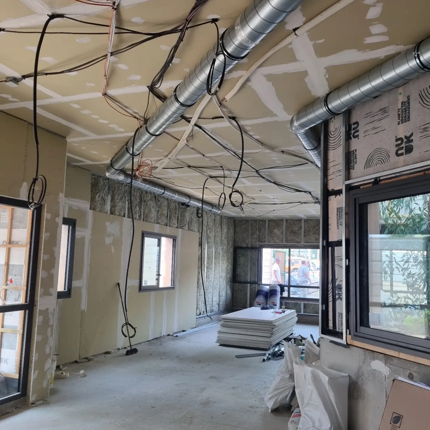 Salle en cours d’aménagement : faux plafond en plaques de plâtre aux joints enduits, traversé de gaines de ventilation, cloisons doublées
