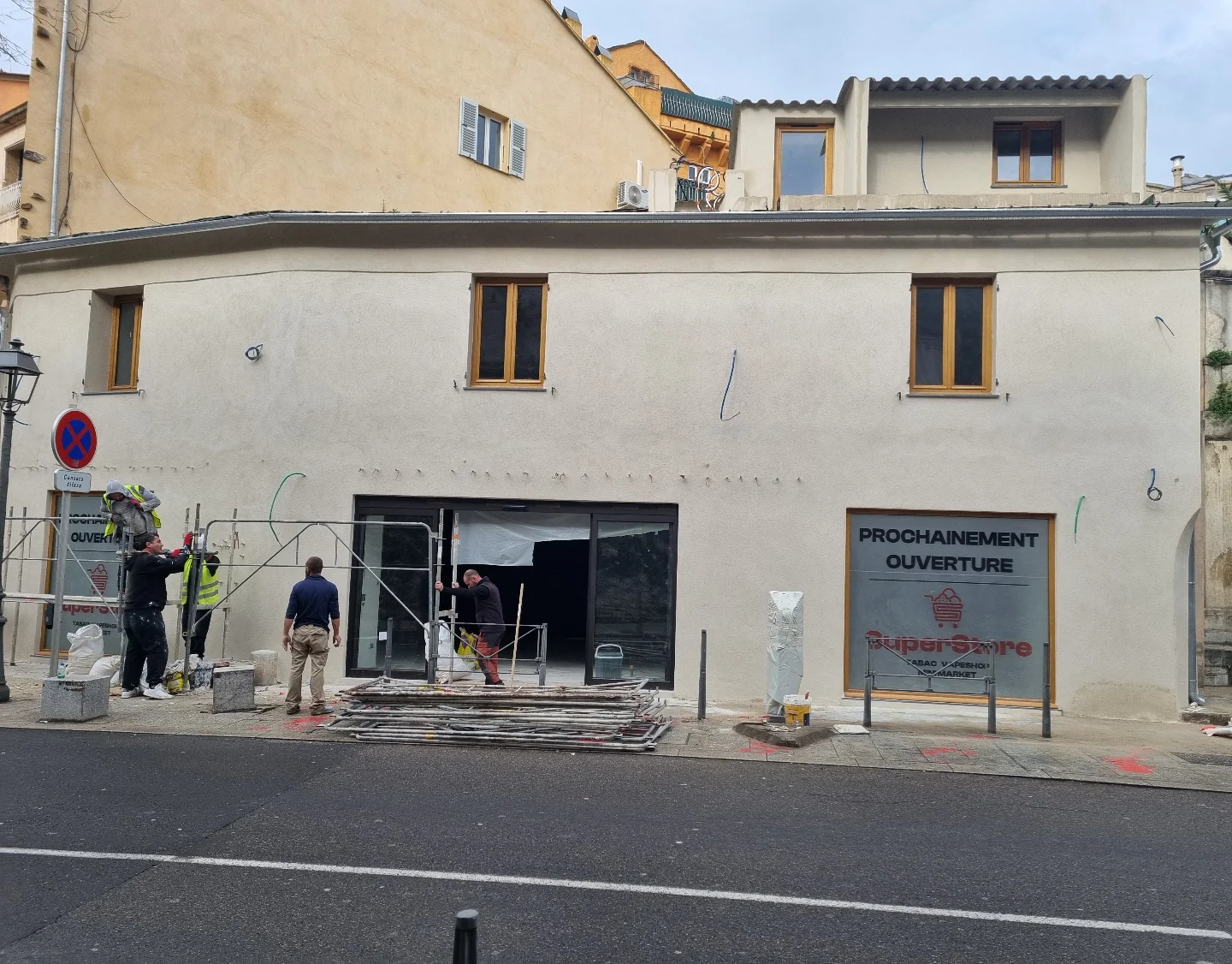 Façade enduite d’un commerce en angle de rue à Bastia, ouvriers sur échafaudage devant la vitrine