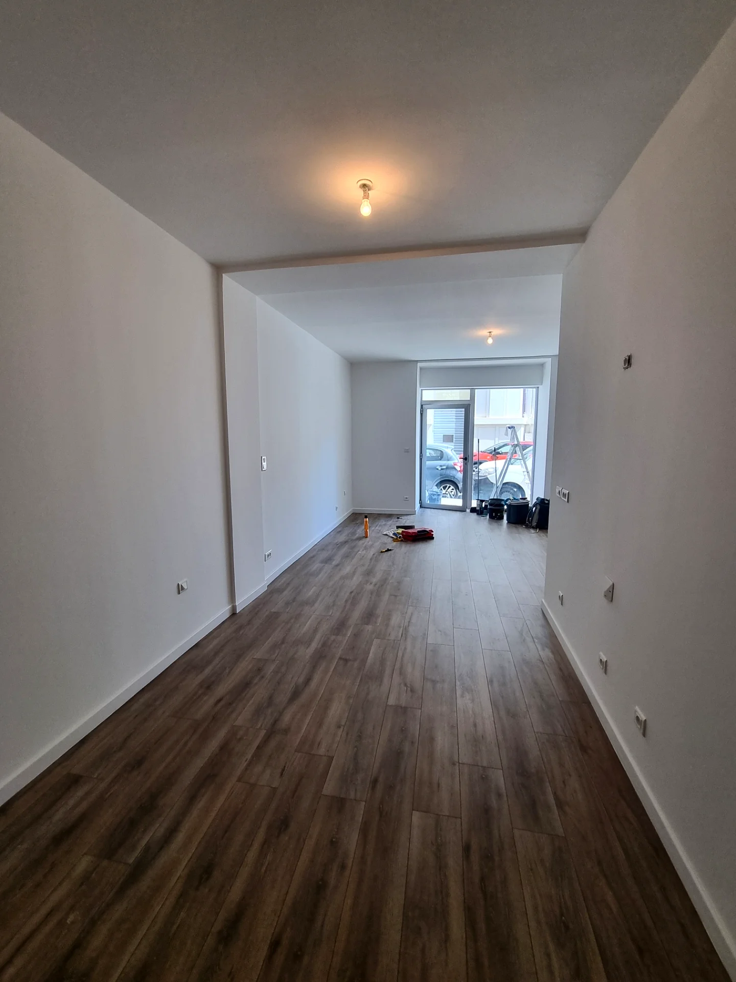 Local commercial rénové : murs blancs, sol stratifié bois, vitrine au fond