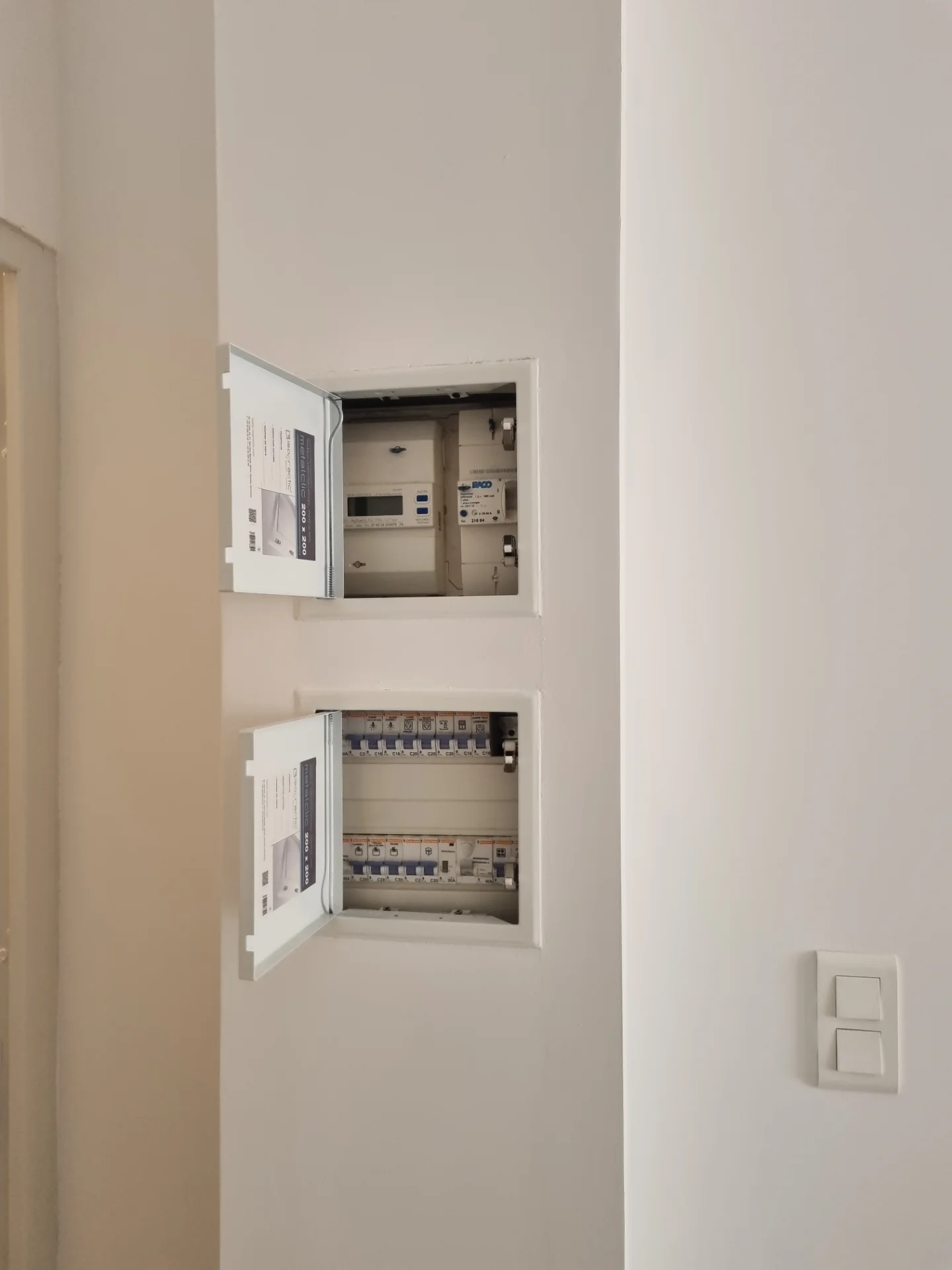 Deux coffrets électriques encastrés dans un mur blanc, trappes ouvertes