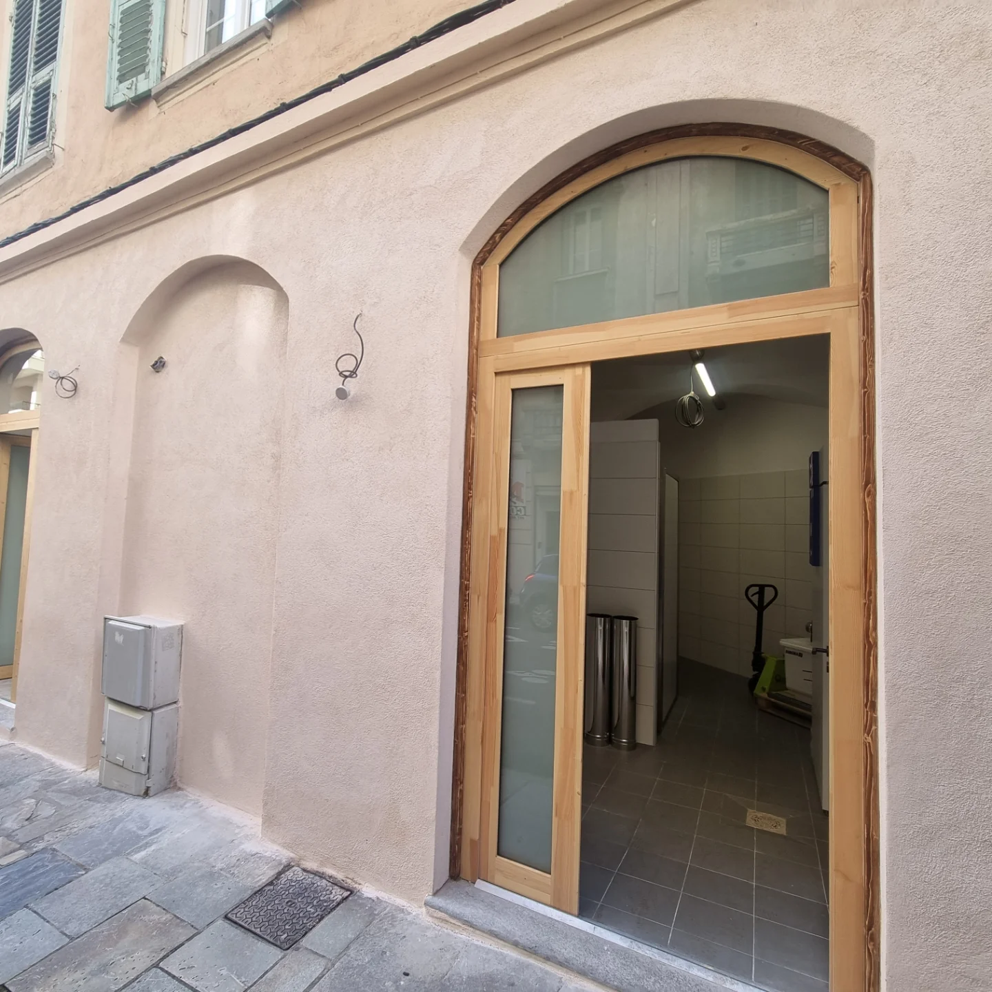Façade enduite d’un local en rez-de-chaussée à Bastia, porte en bois à imposte cintrée et niche en arc