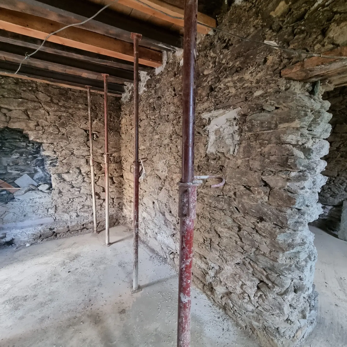 Pièce en pierre apparente avant travaux, plancher bois soutenu par des étais métalliques