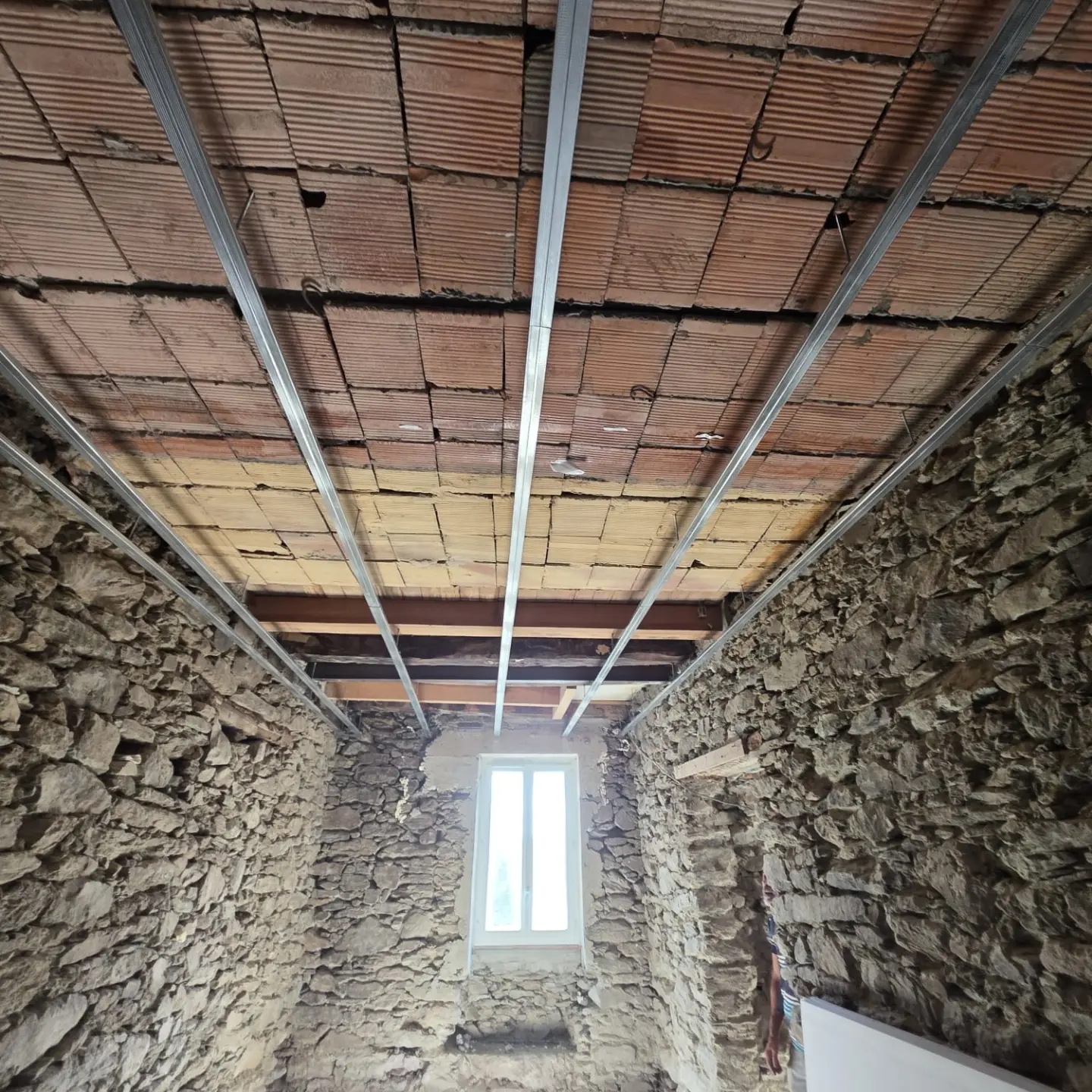 Plafond en briques creuses sous lequel est posée une ossature métallique, murs en pierre et fenêtre au fond