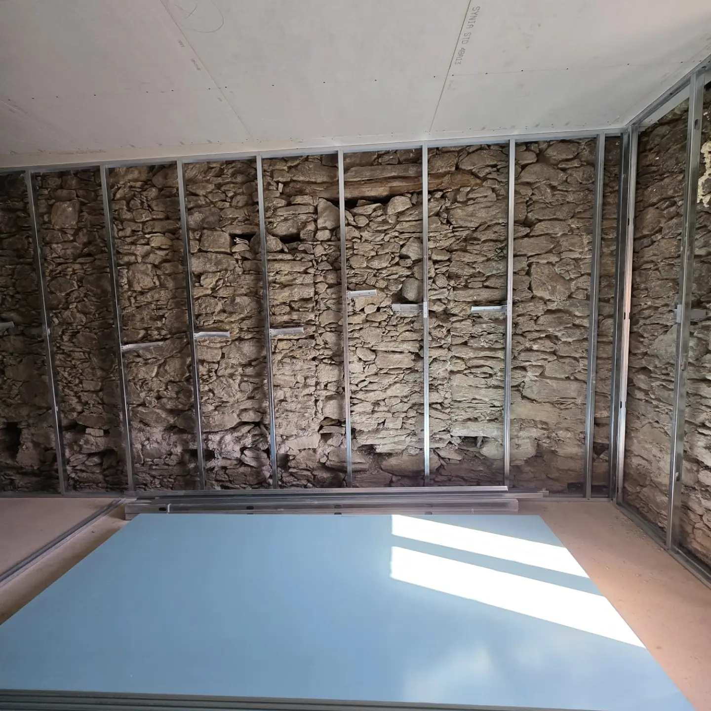 Ossature métallique fixée sur un mur de pierre, plaques de plâtre au sol et plafond déjà posé