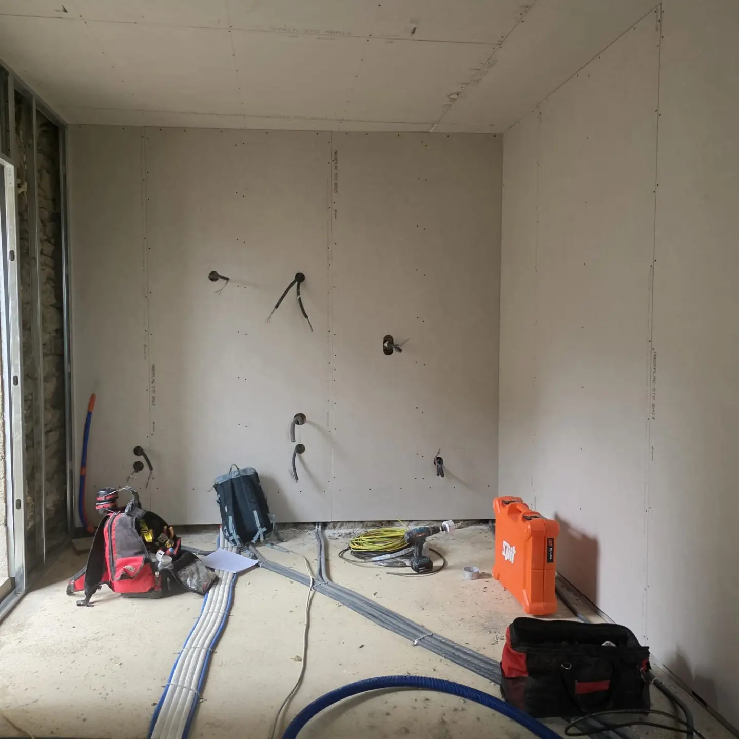 Pièce aux parois en plaques de plâtre, plafond posé et gaines électriques au sol avant finition