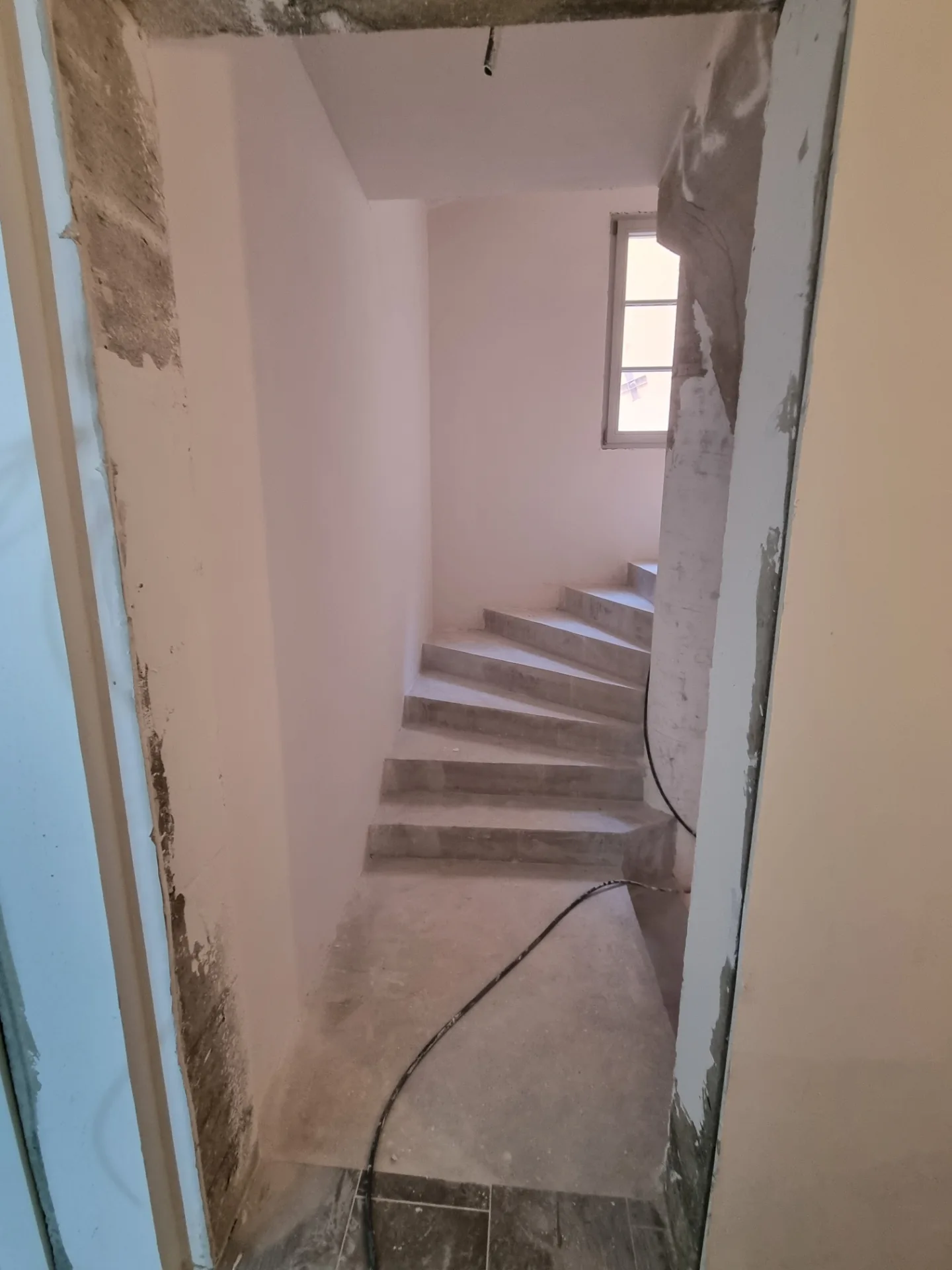 Escalier tournant dans une cage aux murs enduits, éclairée par une fenêtre