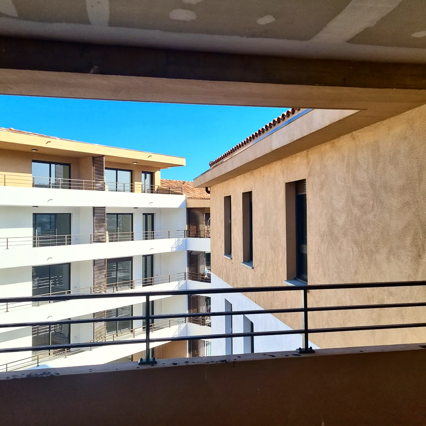 Cour intérieure d’un immeuble de logements neuf, vue depuis une coursive sous un plafond en plaques de plâtre