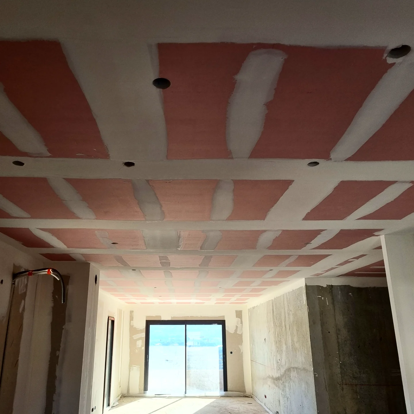Plafond en plaques coupe-feu rouges aux joints bandés, séjour en chantier avec baie vitrée sur la mer